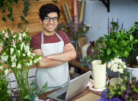 vendedor usando óculos, avental, com braços cruzados em uma empresa de pequeno porte de venda de flores