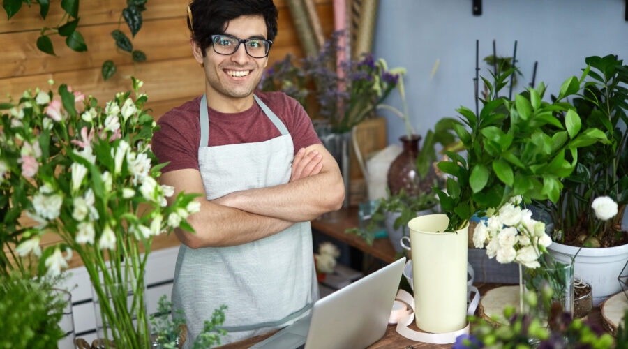 vendedor usando óculos, avental, com braços cruzados em uma empresa de pequeno porte de venda de flores